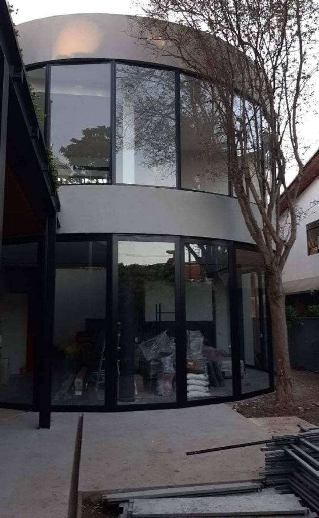 Fachada curva com vidros e portas de perfis escuros durante a instalação.