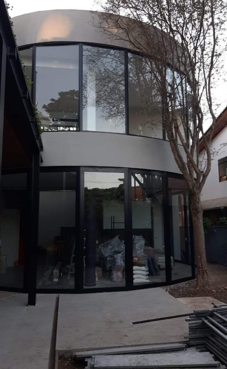 Fachada curva com vidros e portas de perfis escuros durante a instalação.